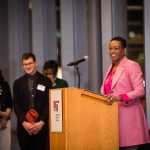 Chancellor Melissa Nobles speaks at a podium, students seen listening in the background.