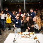 A group of Presidential Fellows take a selfie photo together next to the a 25th Anniversary cake.