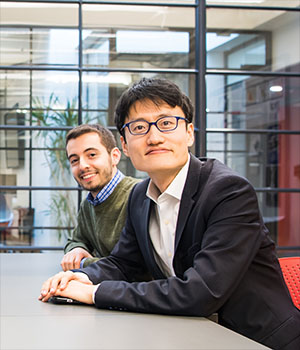Jinhua Zhao and a graduate student sit in front of bright windows.