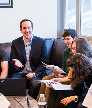 Matthew Shoulders and a group of graduate students laugh as they review documents.