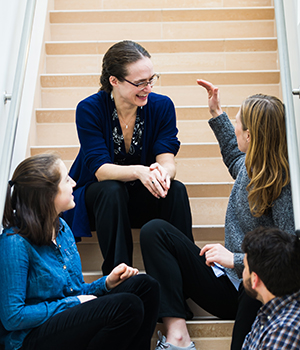 Rebecca Saxe and a group of graduate students sit on stairs and talk.