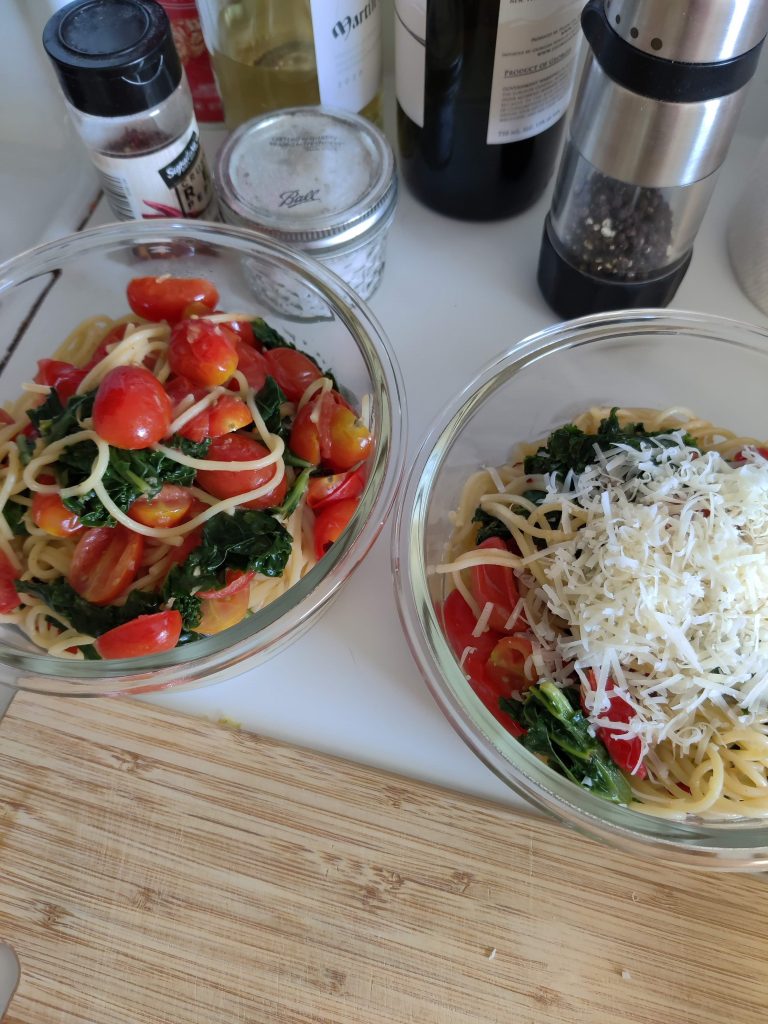 Two bowls of pasta sit on a counter. On the left, the pasta is garnished with tomatoes and leafy vegetables. On the right, it's garnished with the same veggies, but plenty of shredded parmesan cheese.