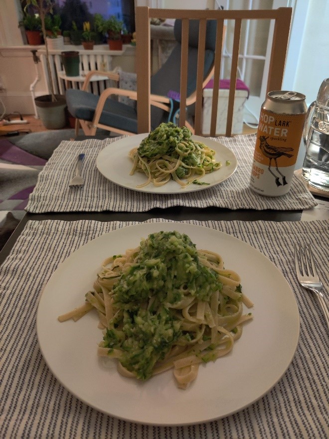 Two generous portions of pasta sit on striped placemats on a dining room table. In the background, chairs and plants are visible.