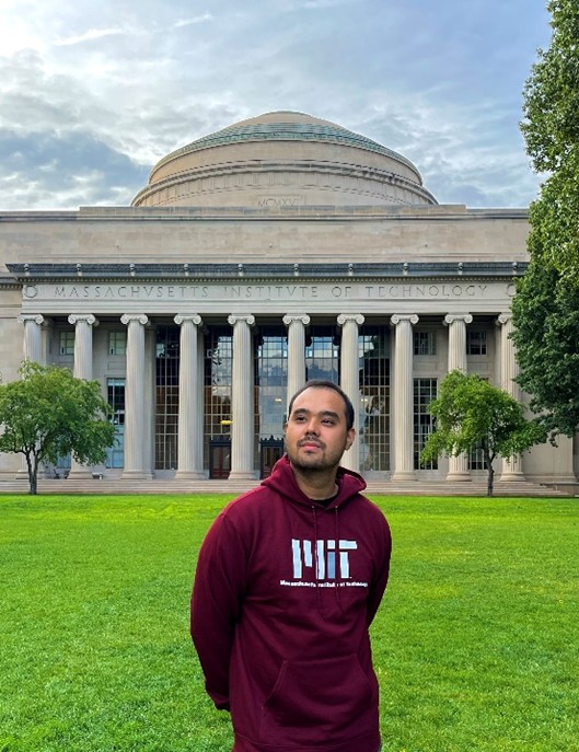 Nauryzkhan stands in front of MIT's Great Dome in Killian Court on a cloudy day.