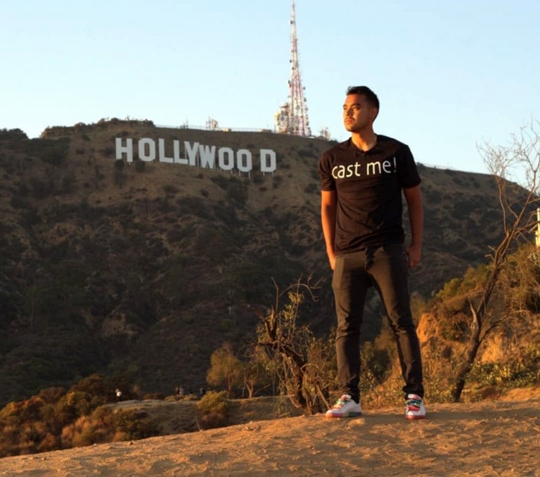 Nauryzkhan poses wearing a "Cast me!" t-shirt on a hill overlooking the Hollywood sign.