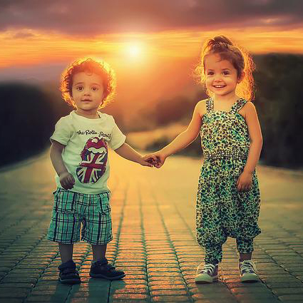 two children in summer clothes holding hands in front of a sunset on a cobblestone road