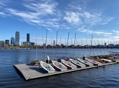 On a clear, blue skies day, a row of sailboats without sails sit on the dock.