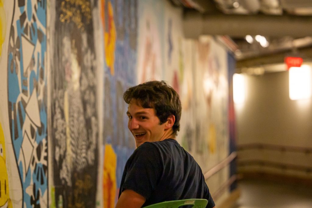 A student grins over their shoulder as their chair rolls past tunnel murals.