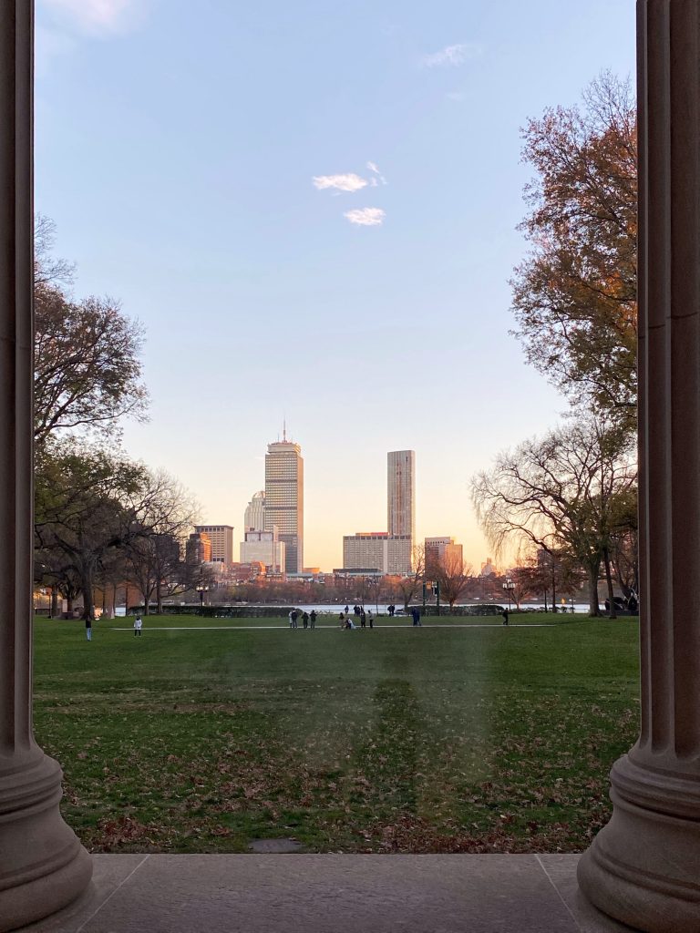Between two of Lobby 10's columns, the Boston skyline glows golden with early sunset light.