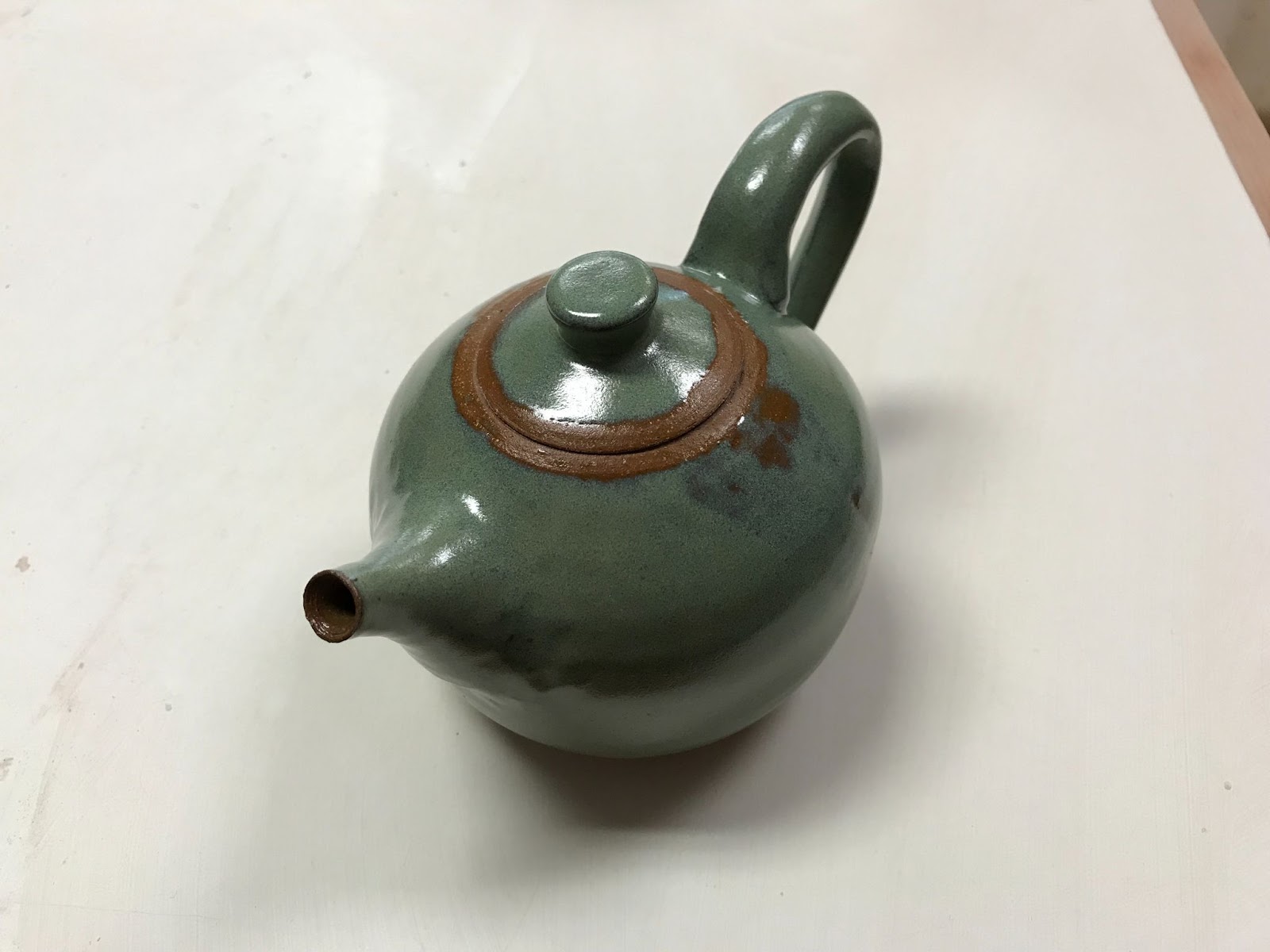 A small, simple teapot with a small spout and a dark green glaze.