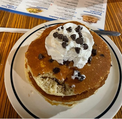 A plate of pancakes topped with a dollop of whipped cream and chocolate chips sits on a table.