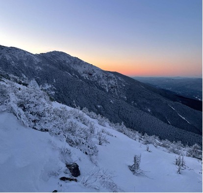 In this view of sunrise over the mountains, snow-covered bushes step up the slope.