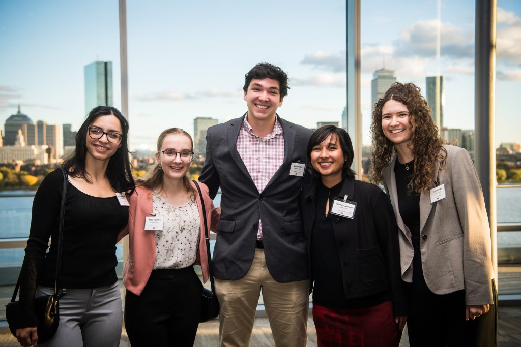 A group of Presidential Fellows stand together, smiling, with the Boston skyline in the background.