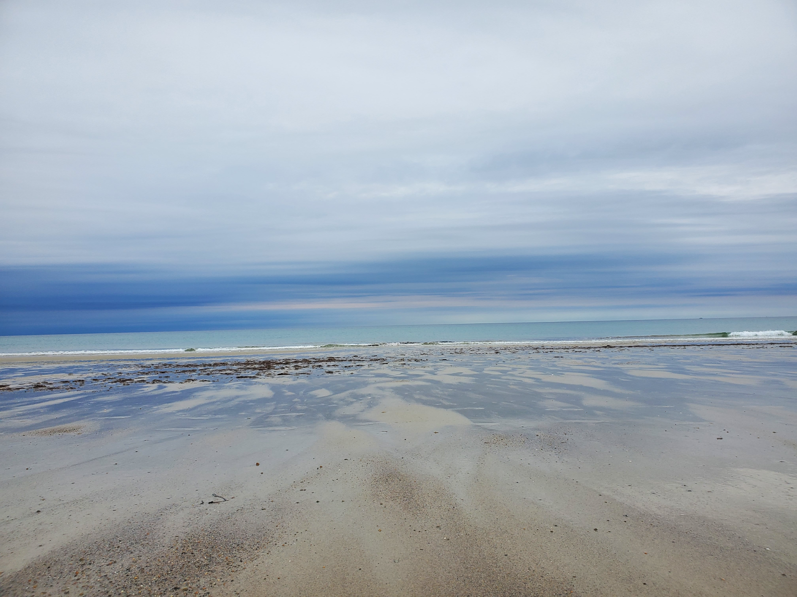 An artistic view of the ocean with a long stretch of beach below and cloudy sky above.