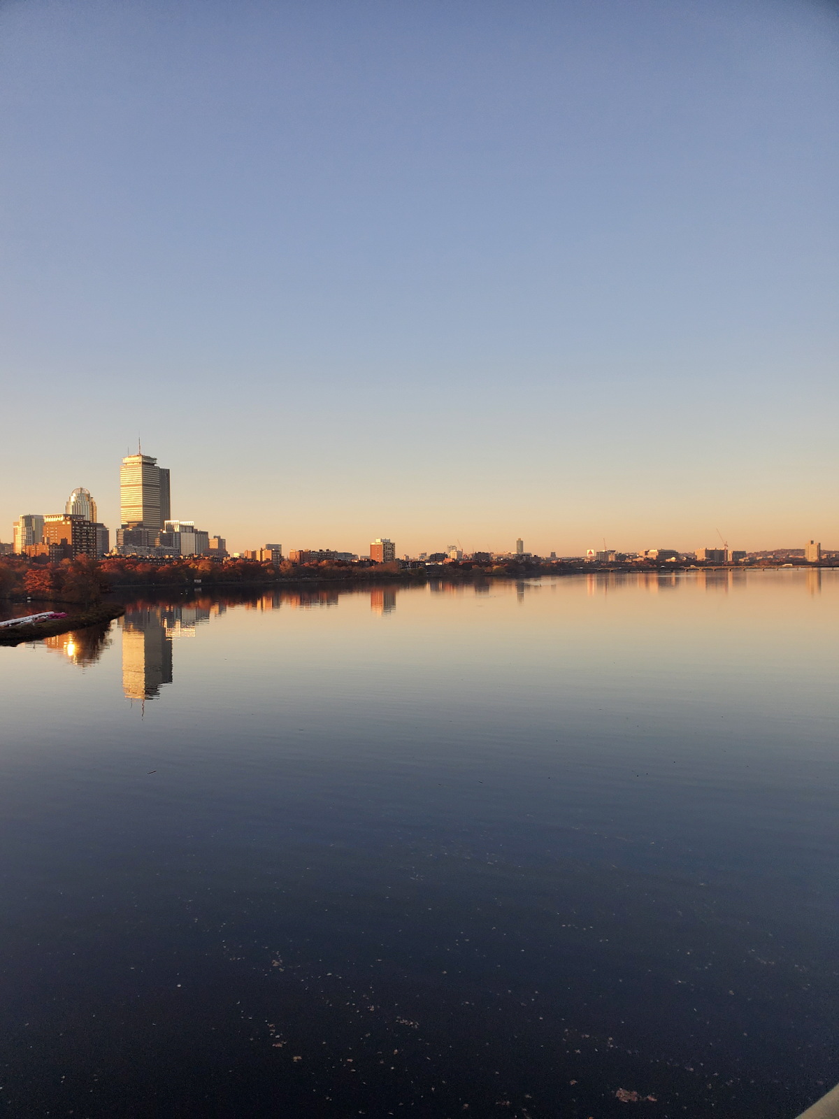 A warm sunset lights the Boston skyline, reflected in a still Charles River.