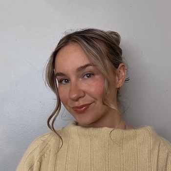 A young woman with brown hair with lighter highlights, wearing a soft yellow sweater