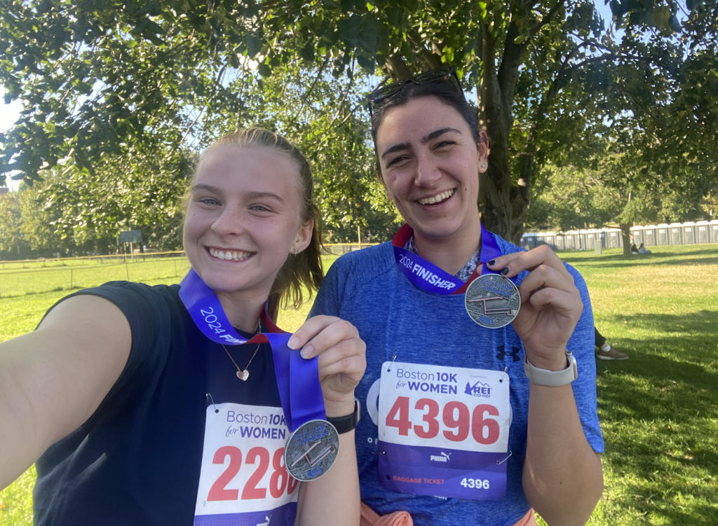 Two runners smile after a race, holding medals