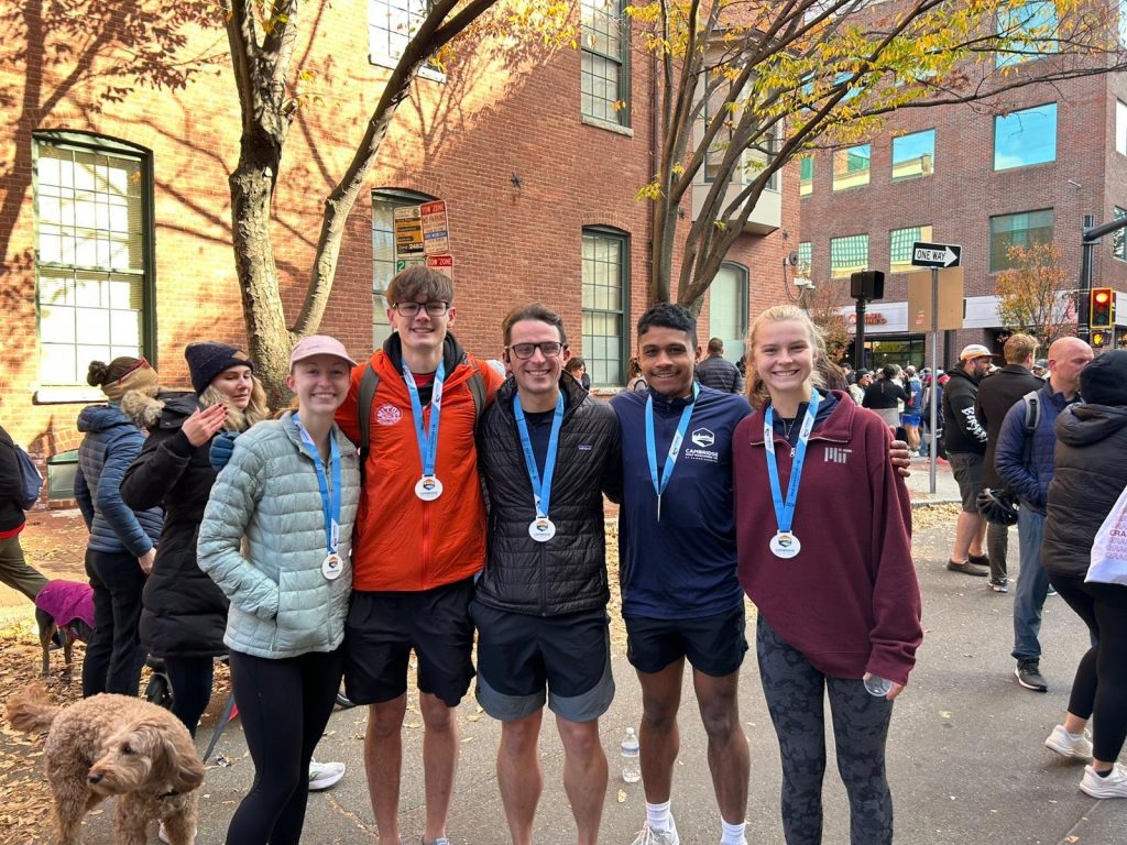 Five runners smile at the camera, wearing medals