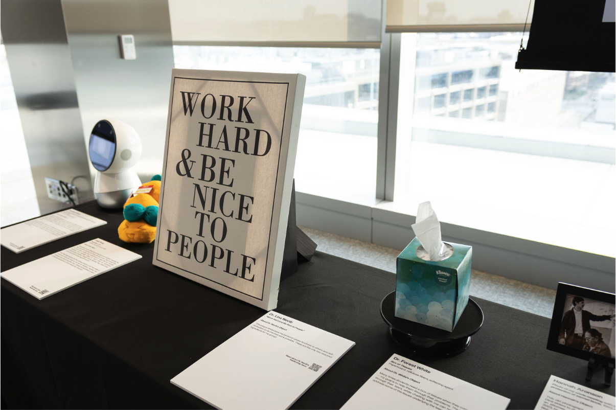 A black-covered table with several objects on it, including a robot, a small stuffed animal, a sign reading 
