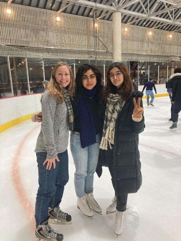 Three female graduate students pose, smiling on an indoor ice rink