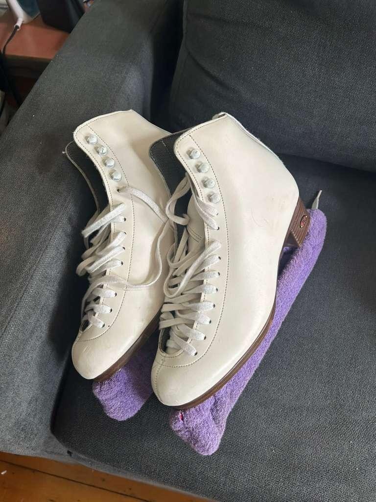 White ice skates rest on a couch with purple blade covers on
